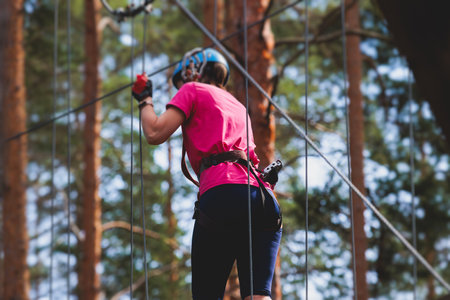 View of high ropes course, process of climbing in amusement acitivity rope park, passing obstacles and zip line on heights in climbing safety equipment gear between the trees om heights in summer dayの写真素材