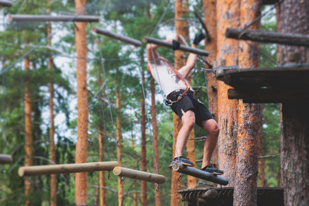 View of high ropes course, process of climbing in amusement acitivity rope park, passing obstacles and zip line on heights in climbing safety equipment gear between the trees om heights in summer dayの写真素材
