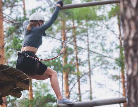 View of high ropes course, process of climbing in amusement acitivity rope park, passing obstacles and zip line on heights in climbing safety equipment gear between the trees om heights in summer dayの写真素材