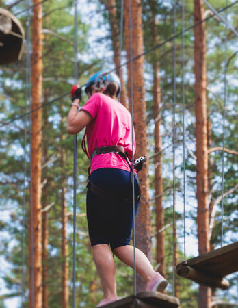 View of high ropes course, process of climbing in amusement acitivity rope park, passing obstacles and zip line on heights in climbing safety equipment gear between the trees om heights in summer dayの写真素材