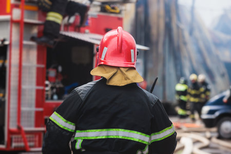 Group of fire men in protective uniform during fire fighting operation in the city streets, firefighters brigade with the fire engine truck vehicle in the background, emergency and rescue serviceの写真素材