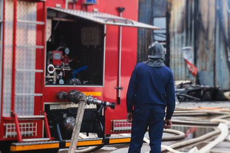 Group of fire men in protective uniform during fire fighting operation in the city streets, firefighters brigade with the fire engine truck vehicle in the background, emergency and rescue serviceの写真素材