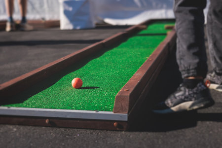 Mini golf course, process of playing miniature golf on a green artificial turf in a summer sunny day, equipment for mini-golf in a golf club resort, club and ballの写真素材