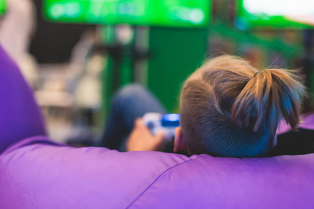 Process of playing video games, video game console with wireless controller, male kid child gamer on a couch bean bag chair, with black joystick in front of big wide screen tv, football video gameの写真素材