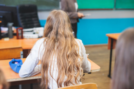 Kids in school writing and taking notes, teens pupils behind desks during the lesson listening to teacher lecture, classroom with students and classmates, group of teenagers during test and examの写真素材