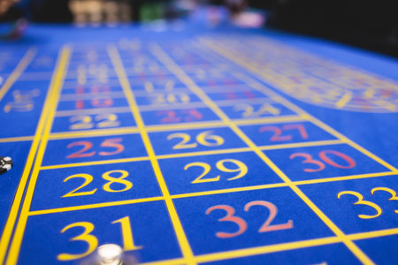 Vibrant casino table with roulette in motion, with casino chips, tokens, the hand of croupier, dollar money and a group of gambling rich people playing bet, blue poker table and deck of cardsの写真素材