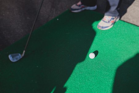 Mini golf course, process of playing miniature golf on a green artificial turf in a summer sunny...