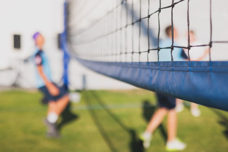 Volleyball game, junior teenage school team of kids play volleyball, players on the outdoor playground with net and green lawn grass court, sports children team during the game, summer sunnyの写真素材