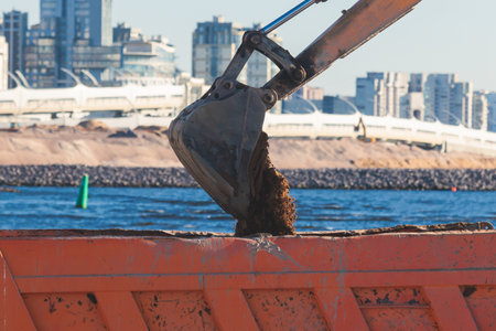Excavator unloading sand into the dump truck on the construction site, excavating and working during road works, backhoe and tipper truck unload road metal and gravel, construction of the new roadの写真素材