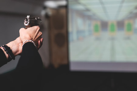 Process of shooting target at the shooting rifle range, women practicing with hand gun pistol at shooting gallery, firearms training, pointing weapon on digital screen, live fire digital targetingの写真素材