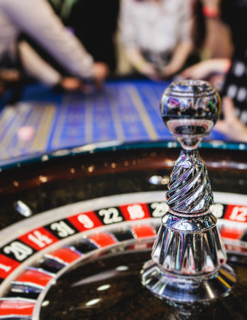 Vibrant casino table with roulette in motion, with casino chips, tokens, the hand of croupier, dollar money and a group of gambling rich people playing bet, blue poker table and deck of cardsの写真素材