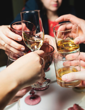 Group of guests celebrate and raise glasses, toasting and cheering with alcohol glasses with wine and champagne in the restaurant on corporate christmas birthday party event or wedding celebrationの写真素材