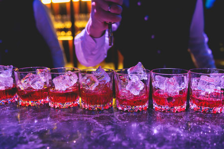 Bartender working, beautiful row line of different colored liquor alcohol cocktails on a party in a bar, and others on catering banquet on event, barman mixing drinks and beverages in a clubの写真素材