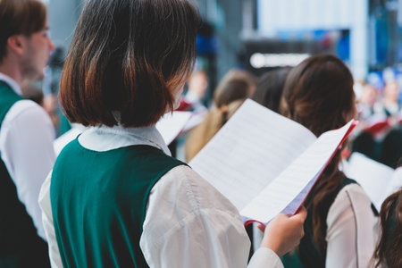 Church choir concert in cathedral, choral artists singing, group of European boys and girls singing in a chorus, students and choristers in white and green uniform performing on stage with conductorの写真素材
