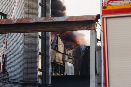 Massive large blaze fire in the city, blazing warehouse factory, storage building burning, firefighters team putting out the fire, firemen on duty, extinguish the fire, arson, burning house damageの写真素材