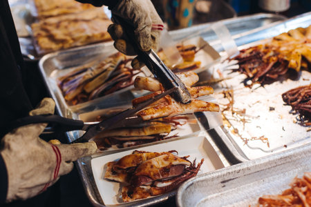 Korean Spicy Grilled Squid, Ojingeo tonggui, grilled octopus tentacles, variety of different street food selection in Seoul, South Korea, night market with local vendor stalls cooking tasty dishesの写真素材