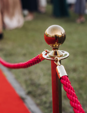 Red carpet with ropes and golden barriers on a luxury party entrance, cinema premiere film festival event award gala ceremony, wealthy rich guests arriving, outdoor decoration elements, summer dayの写真素材