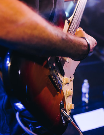 Concert view of an electric guitar player with vocalist and rock band performing in a club, male...