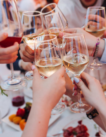 Group of guests celebrate and raise glasses, toasting and cheering with alcohol glasses with wine and champagne in a restaurant on corporate christmas, birthday party prom event or wedding celebrationの写真素材