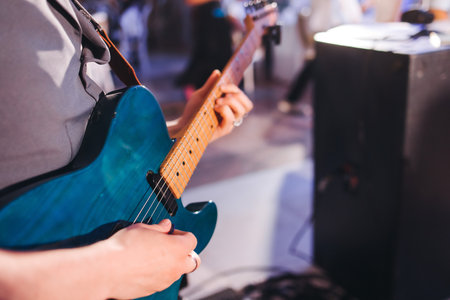 Concert view of an electric guitar player with vocalist and rock band performing in a club, male musician guitarist on stage with audience in a crowded concert show club hall arena, hands on guitarの写真素材