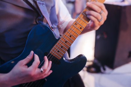 Concert view of an electric guitar player with vocalist and rock band performing in a club, male musician guitarist on stage with audience in a crowded concert show club hall arena, hands on guitarの写真素材
