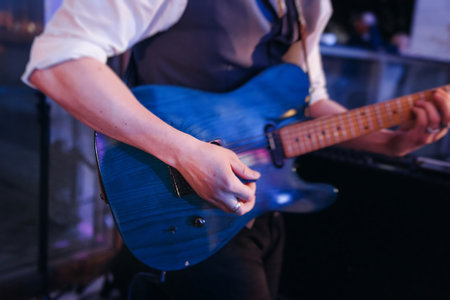 Concert view of an electric guitar player with vocalist and rock band performing in a club, male musician guitarist on stage with audience in a crowded concert show club hall arena, hands on guitarの写真素材