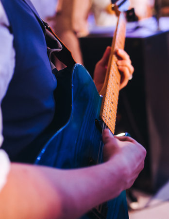 Concert view of an electric guitar player with vocalist and rock band performing in a club, male...