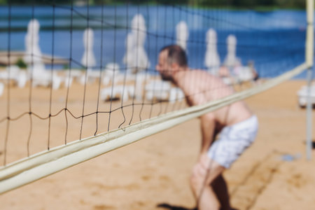 Beach volleyball game, team of adult friends athletes play volleyball by the sea, players on the outdoor playground with net, white sand court field, sports team during the game, in a summer sunny dayの写真素材