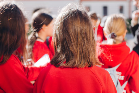 Group of school pupils and students on outdoor excursion tour in the city streets with guide, a docent with a tourist young visitors wearing red, school field trip, urban tour in the summer sunny dayの写真素材