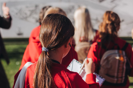 Group of school pupils and students on outdoor excursion tour in the city streets with guide, a docent with a tourist young visitors wearing red, school field trip, urban tour in the summer sunny dayの写真素材