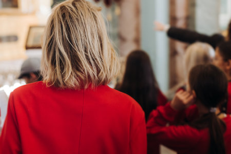 Group of kids children on excursion in a museum gallery, school pupils and students tour with guide, a docent with a tourists, young visitors wearing red, school field trip, art exhibitionの写真素材