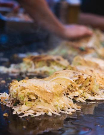 Okonomiyaki Hiroshima-Style - popular Japanese Street Food, pancake with yakisoba noodles, fried egg, and pork, snack selection in Hiroshima, Japan, street market local vendors, teppanyakiの写真素材