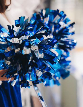 Female cheerleaders group in action, blue and white uniform with pom-pom, audience and hockey teams in the background, performing and supporting during ice hockey game match, cheerleading in ice arenaの写真素材