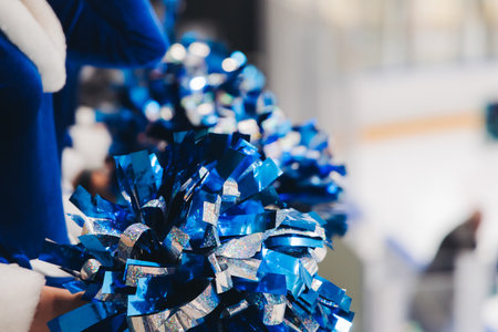 Female cheerleaders group in action, blue and white uniform with pom-pom, audience and hockey teams in the background, performing and supporting during ice hockey game match, cheerleading in ice arenaの写真素材