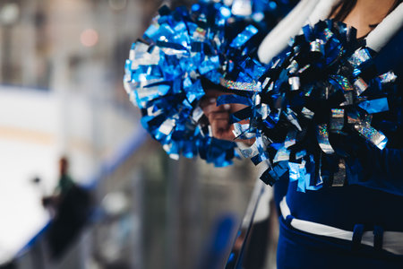 Female cheerleaders group in action, blue and white uniform with pom-pom, audience and hockey teams in the background, performing and supporting during ice hockey game match, cheerleading in ice arenaの写真素材