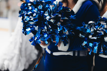 Female cheerleaders group in action, blue and white uniform with pom-pom, audience and hockey teams...