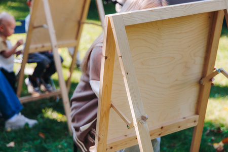 Kids drawing at plein air, group class of talented children with painting easel and wooden canvas during lesson of watercolor painting outdoors in summer, art school class for young teen artistsの写真素材