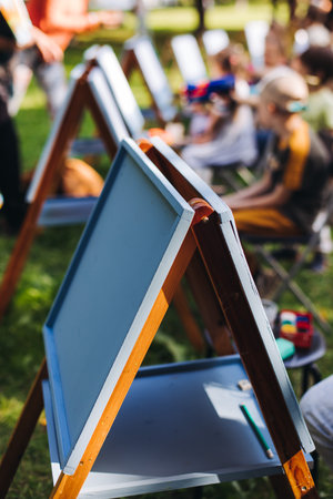 Kids drawing at plein air, group class of talented children with painting easel and wooden canvas during lesson of watercolor painting outdoors in summer, art school class for young teen artistsの写真素材