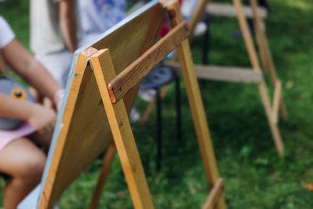 Kids drawing at plein air, group class of talented children with painting easel and wooden canvas during lesson of watercolor painting outdoors in summer, art school class for young teen artistsの写真素材
