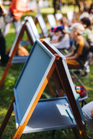 Kids drawing at plein air, group class of children with painting easel and wooden canvas during lesson of watercolor painting outdoors in summer, art school class for young teen artistsの写真素材