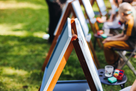 Kids drawing at plein air, group class of talented children with painting easel and wooden canvas during lesson of watercolor painting outdoors in summer, art school class for young teen artists