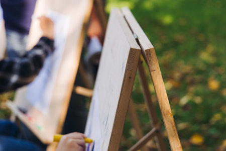 Kids drawing at plein air, group class of talented children with painting easel and wooden canvas during lesson of watercolor painting outdoors in summer, art school class for young teen artistsの写真素材