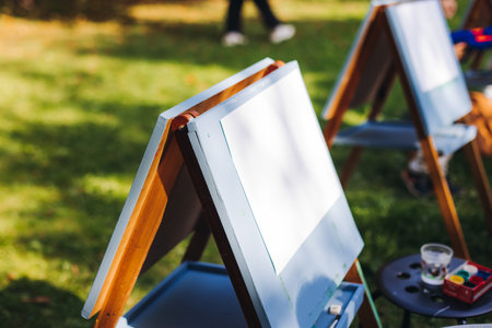 Kids drawing at plein air, group class of talented children with painting easel and wooden canvas during lesson of watercolor painting outdoors in summer, art school class for young teen artistsの写真素材