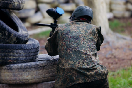 Paintball game, team in camouflage protective uniform with paintball guns and ammunition, strikeball arena battlefield, paintballer aiming and shooting at opponents, airsoft players match tournamentの写真素材