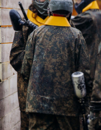 Paintball game, team in camouflage protective uniform with paintball guns and ammunition, strikeball arena battlefield, paintballer aiming and shooting at opponents, airsoft players match tournamentの写真素材