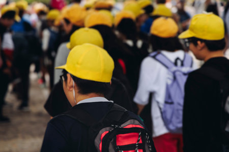 Group of school children students outdoor excursion, guided tour in the city with guide, docent with tourist pupils visitors, wear color caps hats, kids class field trip, urban sightseeing in Japanの写真素材