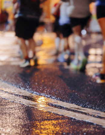 Night marathon runners crowd in the rain, sportsmen participants start running the half-marathon in the city streets with night lighting and illumination, group crowd of sportswomen joggers in motionの写真素材