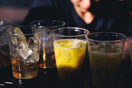 Barman mixing liquor beverages and alcohol drinks in plastic cups, bartender working, beautiful row...