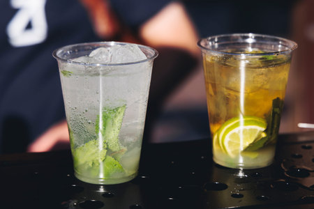 Barman mixing liquor beverages and alcohol drinks in plastic cups, bartender working, beautiful row...