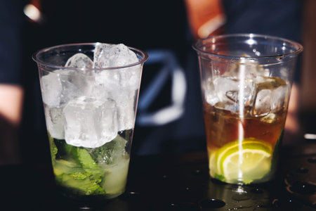 Barman mixing liquor beverages and alcohol drinks in plastic cups, bartender working, beautiful row...